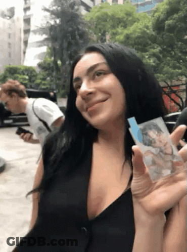 A Woman In A Black Dress Is Holding A Picture Of A Man In A White Shirt GIF