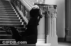 A Woman In A Black Dress Is Kneeling Down On The Stairs In A Black And White Photo . GIF