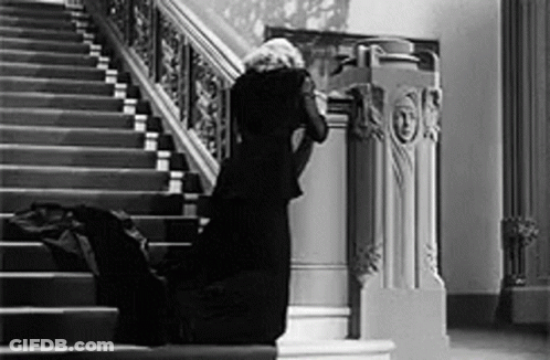 A Woman In A Black Dress Is Kneeling Down On The Stairs In A Black And White Photo . GIF