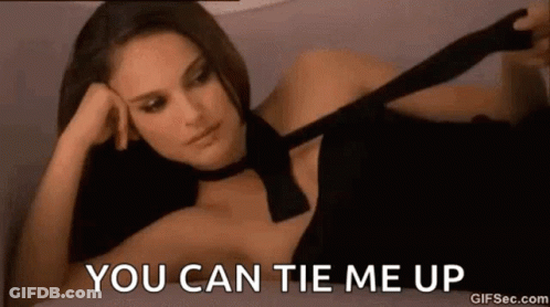 A Woman In A Black Dress Is Laying On A Bed And Tying A Tie . GIF
