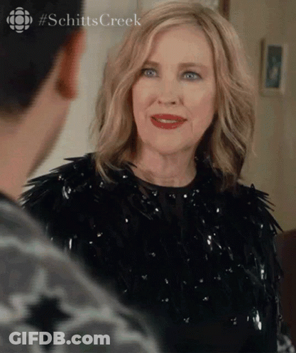 A Woman In A Black Dress Is Looking At A Man In A Room . GIF