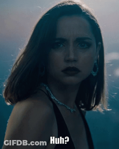 A Woman In A Black Dress Is Looking At The Camera With The Words Huh Below Her GIF