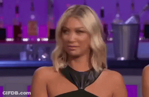 A Woman In A Black Dress Is Making A Funny Face While Sitting In Front Of A Bar . GIF