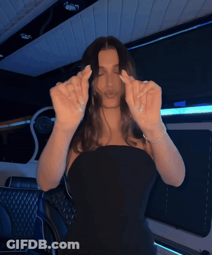 A Woman In A Black Dress Is Making A Heart With Her Fingers GIF