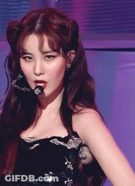 A Woman In A Black Dress Is Singing Into A Microphone On A Stage GIF