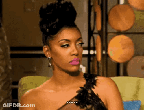 A Woman In A Black Dress Is Sitting In A Chair And Making A Funny Face . GIF