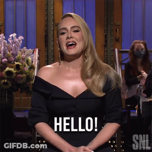 A Woman In A Black Dress Is Sitting In A Chair And Saying Hello GIF