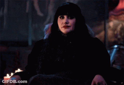 A Woman In A Black Dress Is Sitting In A Chair With Candles In The Background . GIF