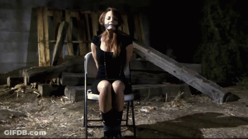 A Woman In A Black Dress Is Sitting In A Chair With Duct Tape On Her Mouth GIF