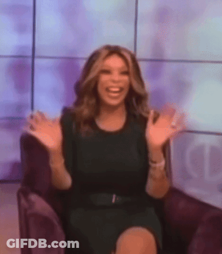 A Woman In A Black Dress Is Sitting In A Chair With Her Arms Outstretched And Smiling . GIF