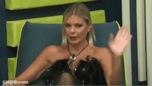 A Woman In A Black Dress Is Sitting In A Chair With Her Hand Up . GIF