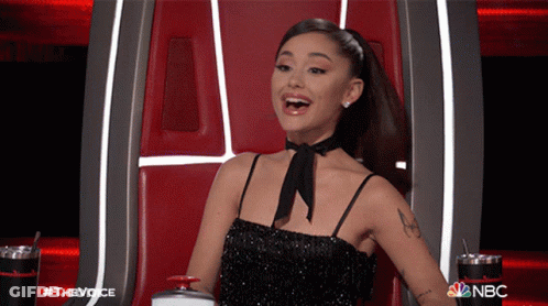 A Woman In A Black Dress Is Sitting In A Chair With The Nbc Logo Behind Her GIF