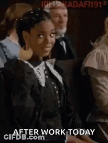 A Woman In A Black Dress Is Sitting In A Crowd Of People And Looking At The Camera . GIF
