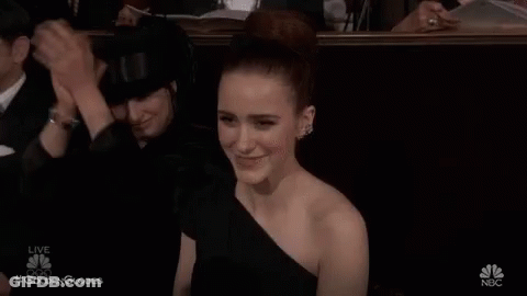 A Woman In A Black Dress Is Sitting In A Theatre Applauding A Man . GIF