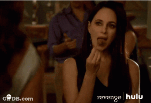 A Woman In A Black Dress Is Sitting In Front Of A Man In A Purple Shirt And A Sign That Says Revenge Hulu GIF