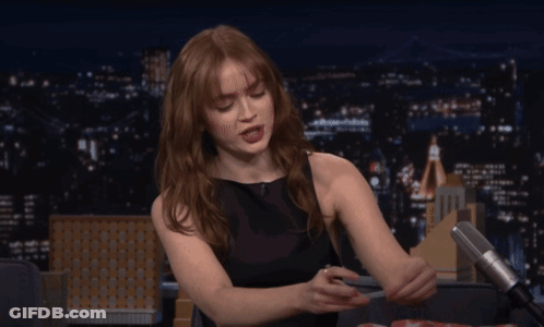 A Woman In A Black Dress Is Sitting In Front Of A Microphone At Night GIF