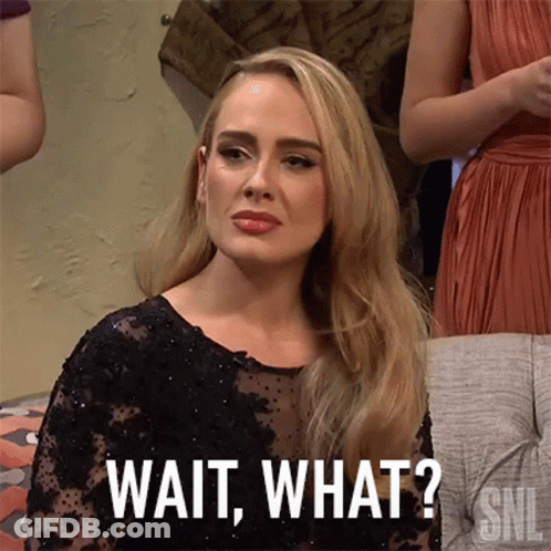 A Woman In A Black Dress Is Sitting On A Couch And Says Wait What . GIF