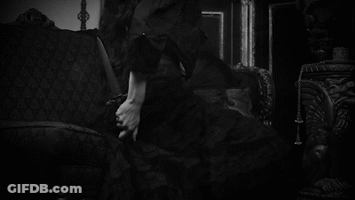 A Woman In A Black Dress Is Sitting On A Couch In A Room . GIF