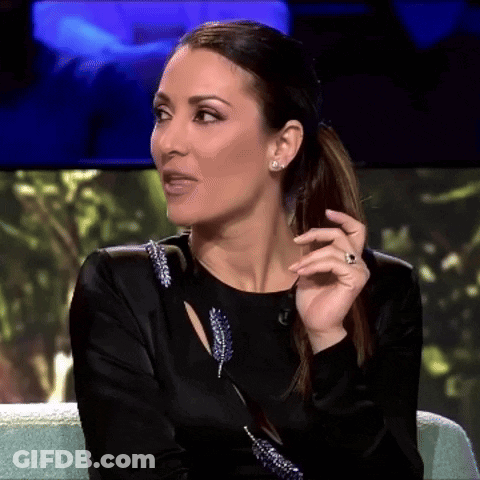 A Woman In A Black Dress Is Sitting On A Couch With Her Hand On Her Face GIF