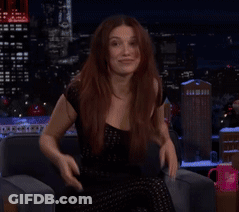 A Woman In A Black Dress Is Sitting On A Couch With Her Hands On Her Face GIF