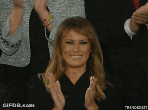 A Woman In A Black Dress Is Smiling And Clapping In Front Of A Crowd GIF