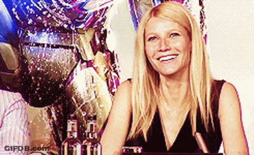 A Woman In A Black Dress Is Smiling In Front Of A Statue GIF