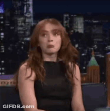 A Woman In A Black Dress Is Smiling While Sitting On A Couch In Front Of A City Skyline . GIF