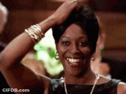 A Woman In A Black Dress Is Smiling With Her Hand On Her Head . GIF