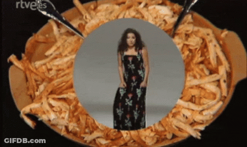 A Woman In A Black Dress Is Standing In A Bowl Of Shredded Meat GIF
