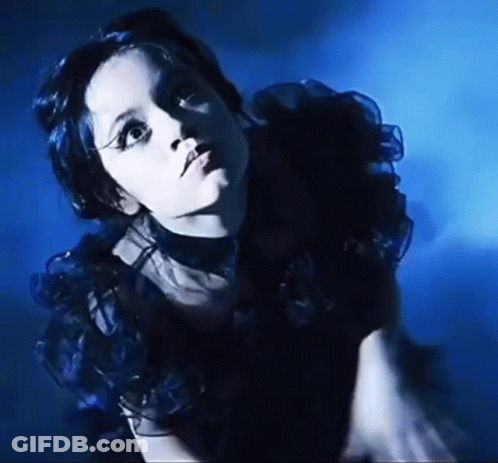 A Woman In A Black Dress Is Standing In A Dark Room . GIF