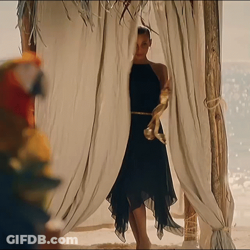 A Woman In A Black Dress Is Standing In A Gazebo On The Beach GIF