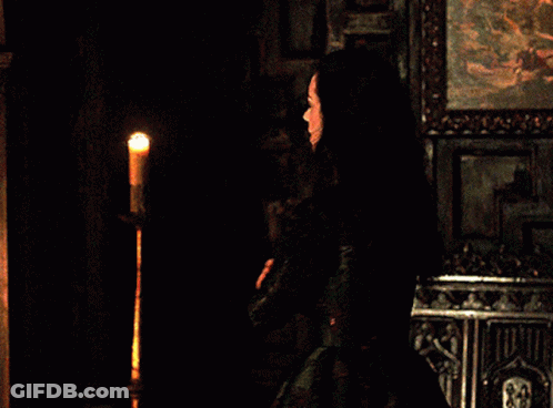 A Woman In A Black Dress Is Standing In Front Of A Candle GIF