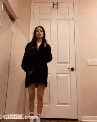A Woman In A Black Dress Is Standing In Front Of A Door GIF