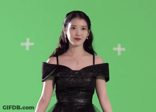 A Woman In A Black Dress Is Standing In Front Of A Green Background GIF
