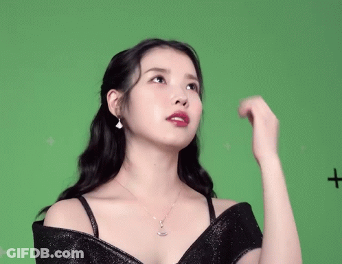 A Woman In A Black Dress Is Standing In Front Of A Green Screen With A Plus Sign On It GIF