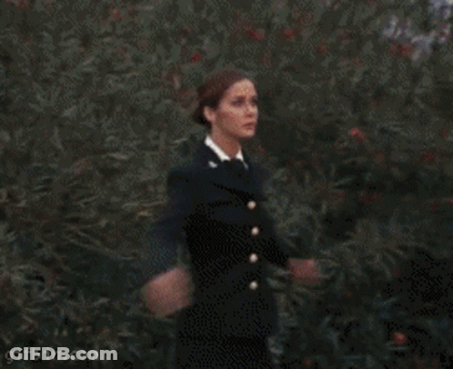 A Woman In A Black Dress Is Standing In Front Of A Red Circle That Says Gifbin.com On It GIF