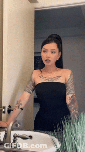 A Woman In A Black Dress Is Standing In Front Of A Sink GIF