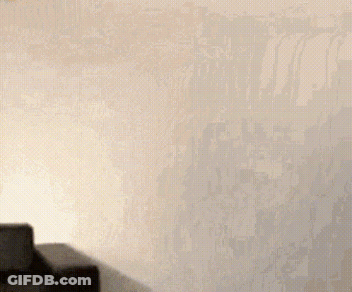 A Woman In A Black Dress Is Standing In Front Of A White Wall With A Sign That Says ' By Suzy ' On It GIF