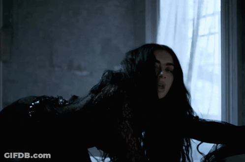 A Woman In A Black Dress Is Standing In Front Of A Window GIF