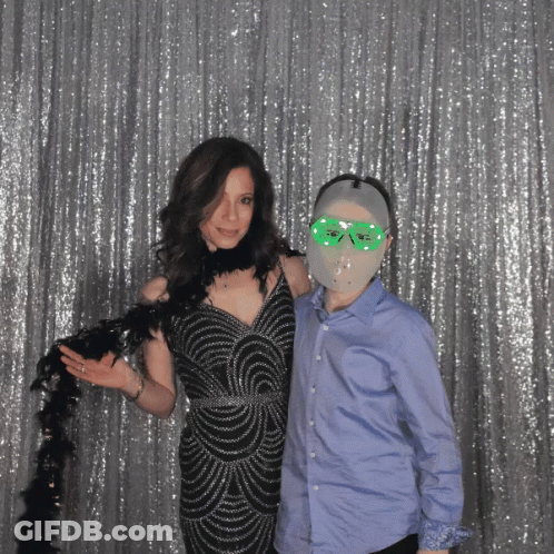 A Woman In A Black Dress Is Standing Next To A Boy Wearing A Mask GIF