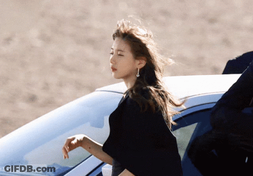 A Woman In A Black Dress Is Standing Next To A Car GIF