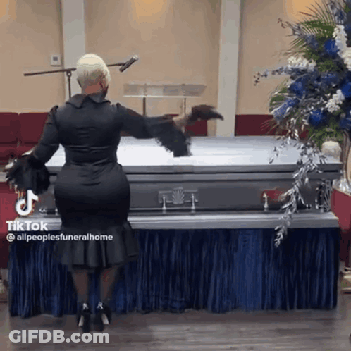 A Woman In A Black Dress Is Standing Next To A Coffin In A Church . GIF