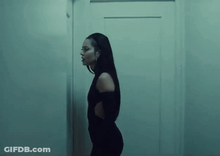 A Woman In A Black Dress Is Standing Next To A Door In A Dark Room . GIF