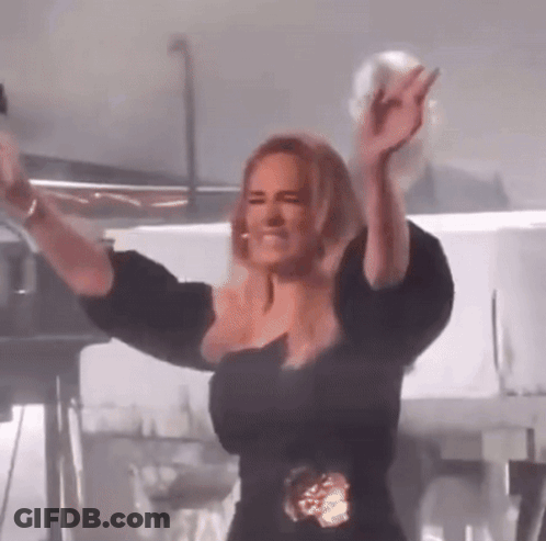 A Woman In A Black Dress Is Standing On A Stage With Her Arms In The Air . GIF