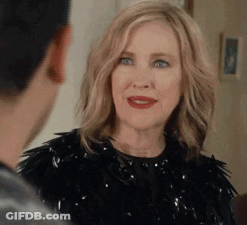 A Woman In A Black Dress Is Talking To A Man In A Room . GIF