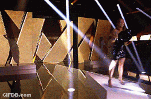 A Woman In A Black Dress Is Walking Down A Stage GIF