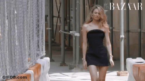 A Woman In A Black Dress Is Walking Down A Street . GIF