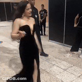 A Woman In A Black Dress Is Walking In A Room . GIF