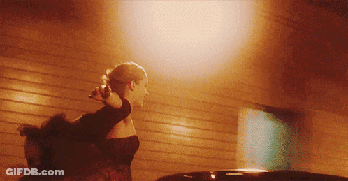 A Woman In A Black Dress Is Walking In Front Of A Building GIF