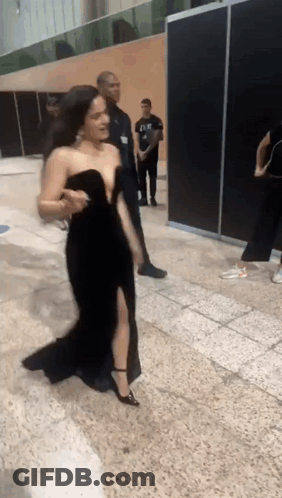 A Woman In A Black Dress Is Walking On A Tiled Floor GIF
